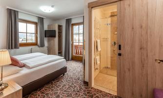 A modern hotel room with a large double bed and a bathroom area. The room has bright windows and a cozy atmosphere.