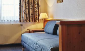 A cozy room with a blue sofa and a lamp. Three pictures hang on the wall, and the room has curtains.