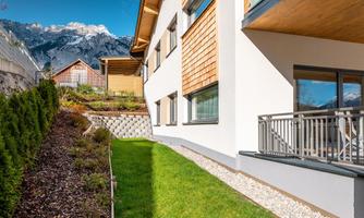 A modern house with wooden cladding and large windows. The garden is well-kept and offers a beautiful view of the mountains.