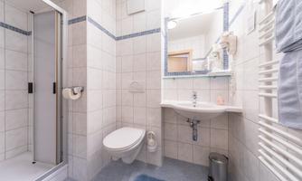 A modern bathroom with a shower, a toilet, and a sink. The walls are tiled in light colors and there is a small doormat on the floor.