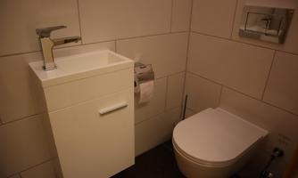 A modern bathroom with a white sink and a toilet bowl. The walls are lined with light tiles.