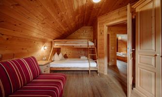 A cozy room with wood paneling and a bunk bed. There is a red couch and access to another room.