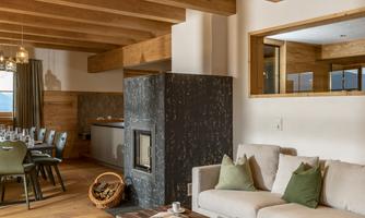 A cozy living room with wooden beams and a modern fireplace. A stylish couch and a wooden table complement the inviting atmosphere.