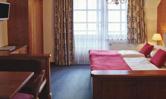 A cozy hotel room with a double bed and red pillows. Generous windows provide plenty of daylight and a pleasant atmosphere.