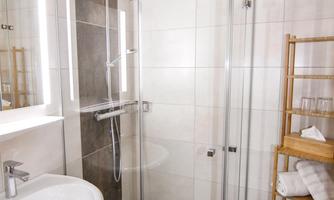 A modern bathroom with a glass shower and a sink. Towels are neatly arranged on a wooden shelf.