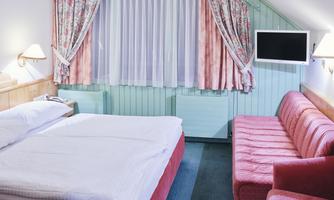 A cozy room with a large bed, a red sofa, and a television. The walls are painted in soft colors with floral curtains.