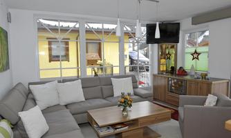 A modern living room with a comfortable couch and plenty of natural light. Large windows offer a view of a colorful outdoor area.