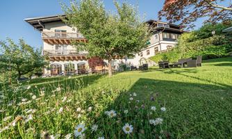 A charming house with a well-kept garden. Colorful flowers and green trees surround the terrace.