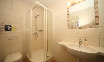 A modern bathroom with a shower, a sink, and a large mirror. The walls are light tiled and the fixtures are functional.