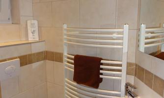 A modern bathroom with tiles and a towel rack. On the right is a sink and a small mirror.