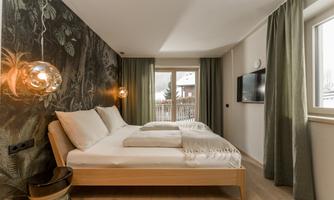 A modern bedroom with a double bed and stylish lighting elements. Large windows let in plenty of daylight and offer a view outside.
