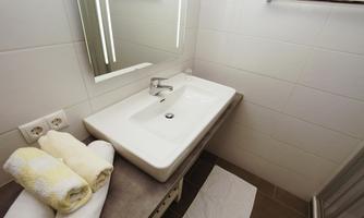 A modern bathroom with an elegant sink and large mirror lighting. Clean towels and a grooming towel are ready.