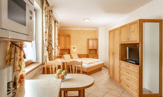 A cozy room with wooden furniture and an adjoining kitchen. The room is bright and friendly, with a large window and a table.
