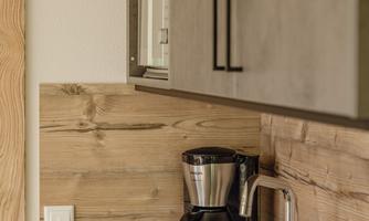 A modern kitchen corner with a wooden shelf and a coffee machine. The space has a cozy atmosphere with simple design.