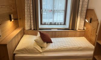 A simple bedroom with a single bed and wooden paneling. The window lets in plenty of daylight, and there is a cozy atmosphere.