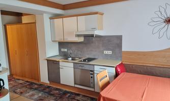A modern kitchen with bright cabinets and a cooking area. A table with a red tablecloth and chairs is also visible.