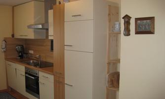 A modern kitchen with bright cabinets and wooden details. It is well-equipped with a stove, sink, and an open shelf.