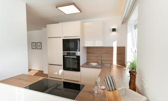 A modern kitchen with light furniture and wooden details. It is well-equipped and has plenty of natural light.