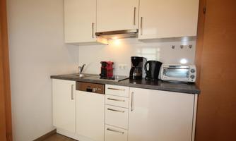 A modern kitchen corner with white cabinets and a dark countertop. A kettle, a toaster, and a coffee machine are visible.