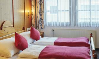 A cozy room with two single beds and red pillows. Large windows let in plenty of daylight.