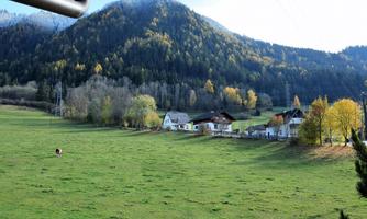 A picturesque landscape with gentle hills and colorful trees in the background. In the foreground, some traditional houses and a green meadow can be seen.