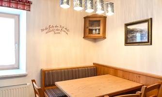 A cozy dining area with a wooden table and chairs. The walls are light, and a modern lamp provides pleasant lighting.