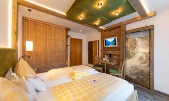 A modern hotel room with wooden furniture and a cozy atmosphere. There are two beds, a television, and a small workspace.