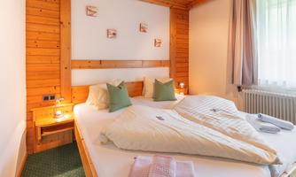 A cozy bedroom with wooden paneling and a large double bed. The color-coordinated cushions and gentle light create an inviting atmosphere.