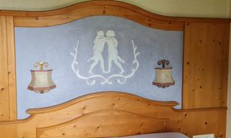 A decorative wooden headboard with a blue background. It features two dancing figures and adorned lanterns.