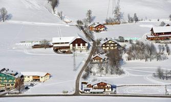 A snowy landscape with several houses and trees. The surroundings are calm and idyllic.