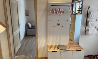 A modern entrance with a shoe cabinet and a coat rack. In the background, a living room with a gray sofa can be seen.