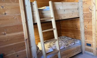 A cozy room with a wooden bunk bed. The walls are also made of wood, creating a rustic atmosphere.