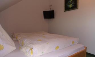 A simple bedroom with a double bed and colorful bed covers. A small television and a picture are hanging on the wall.