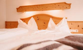 A cozy bedroom with a wooden headboard and white pillows. The bedding is bright and inviting, perfect for relaxation.