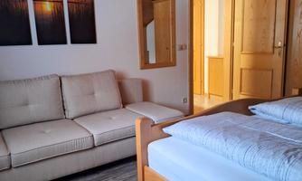 A cozy room with a comfortable sofa and a double bed. Pictures of a sunset are hanging on the wall.