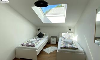 A bright bedroom with two single beds and a later skylight. The floor is wooden and there is a bedside table between the beds.