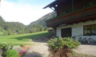 A picturesque house in a green mountain landscape. The path is lined with flowers, and bicycles stand in the foreground.