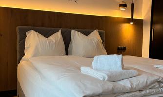 A modern bedroom with a comfortable bed and elegant wall decor. The soft lighting creates a relaxed atmosphere.
