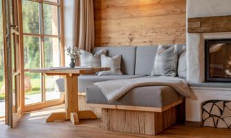 A cozy living room with a gray couch and wooden walls. A table stands next to the couch, and large windows let in plenty of light.