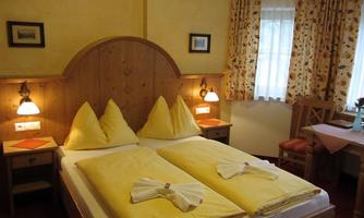 A cozy room with two beds and yellow bedspreads. The walls are bright, and the windows are adorned with floral curtains.