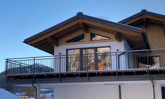 A modern house with a sloped roof and a balcony. The snow lies all around the building, and the windows reflect the sunlight.