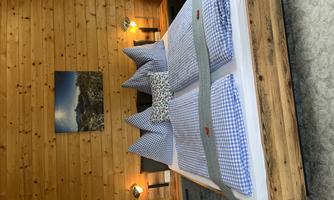 A cozy bedroom with a large bed and checkered pillows. The walls are made of wood, and there is soft lighting from a lamp.