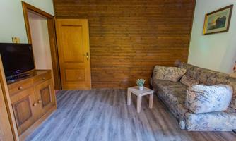 A cozy living room with a sofa and a small table. The walls are partially made of wood, and there is a television.
