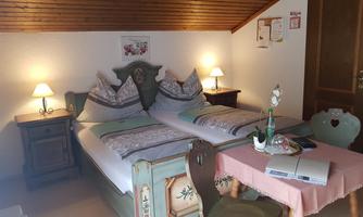 A cozy bedroom with two beds and traditional wooden furniture. The soft lighting creates an inviting atmosphere.