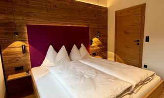 A cozy bedroom with a large bed and modern wooden details. The warm lighting and minimalist style create a relaxed atmosphere.