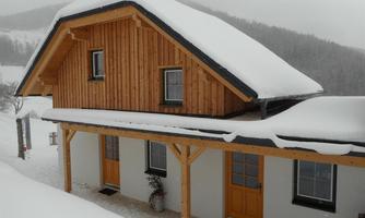 A cozy wooden house in the snow, surrounded by a winter landscape. The eaves are covered with a thick layer of snow.