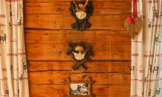 A rustic wooden wall with decorative antler trophies. Next to the trophies, curtains with a traditional pattern hang.