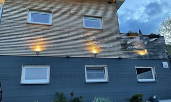 A modern building with a wooden facade and elegant windows. It is illuminated in the evening and displays a friendly atmosphere.
