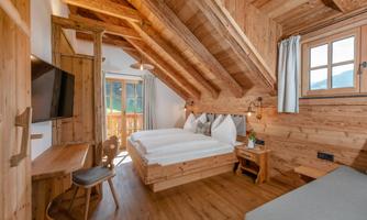 A cozy bedroom with wood paneling and a large window. There is a double bed, a desk, and a television.