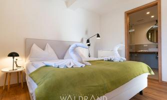 A modern bedroom with a comfortable double bed and green bedding. The room features soft lighting and a stylish table.